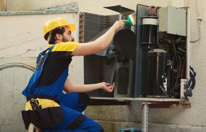 Skilled HVAC engineer removing layer of dust from blower fan to prevent ventilation system damage. Precise mechanic cleaning internal parts to stop risk of condenser overheating